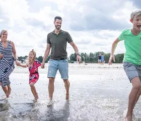 Lachende familie met kinderen spettert en speelt in het ondiepe water bij Landal Marissa, genietend van strand en meer.