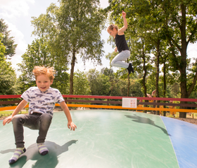 Kinderen springen hoog in de lucht op de grote airtrampoline op Landal Miggelenberg.
