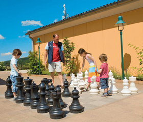 Een vader speelt samen met zijn kinderen met het reusachtige buitenschaakspel op het terras van Landal Mont Royal.