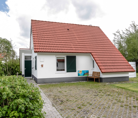 De voorkant van een comfortabele, witte vakantiebungalow met rode dakpannen op Landal Natuurdorp Suyderoogh.