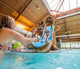 Een meisje glijdt lachend van de glijbaan in het overdekte zwembad en plonst in het water bij haar moeder op vakantiepark Landal Rabbit Hill.