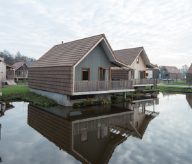 Twee moderne, houten waterwoningen met veranda's die direct aan het kabbelende water van de Reeuwijkse Plassen liggen.