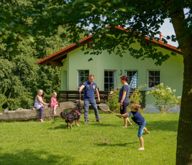 Gezin speelt en maakt een radslag in de tuin voor hun vakantiewoning op vakantiepark Landal Salztal Paradies.