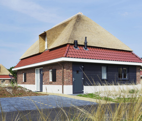 Een luxe, vrijstaande vakantiewoning met een rieten dak en een terras, gelegen in het duingras van vakantiepark Landal Sluftervallei op Texel.