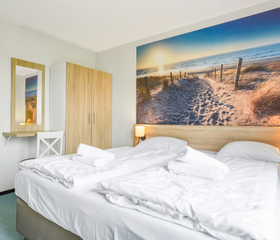 Comfortabele slaapkamer met een tweepersoonsbed en sfeervol fotobehang van een duinlandschap in een huisje op Landal Sneekermeer.