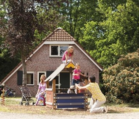Kinderen spelen met hun ouders bij een speeltoestel met glijbaan in de tuin van een kinderbungalow op Landal Stroombroek.