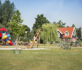De ruime buitenspeeltuin met een groot grasveld en diverse houten speeltoestellen op Landal Waterparc Veluwemeer.