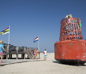 Kinderen spelen op het brede Noordzeestrand van Terschelling bij een grote rode boei.