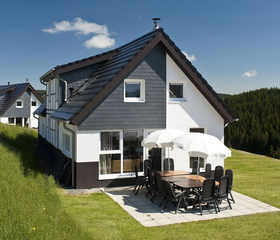 De buitenkant van een modern vakantiehuis bij Landal Winterberg in Sauerland, met een ruim terras en tuinmeubilair op een zonnige dag.