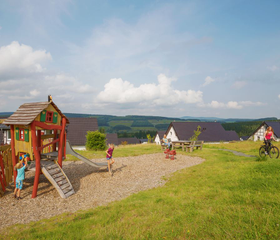 Kinderen spelen op de houten klimtoestellen in de buitenspeeltuin van Landal Winterberg, met uitzicht over het heuvelachtige landschap.