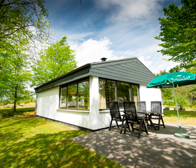Een vrijstaande, witte bungalow van Landal Wirfttal met een terras en tuinmeubilair, gelegen in een groene, bosrijke omgeving.