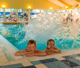 Twee jongens lachen en spetteren in het binnenzwembad van Landal Wirfttal, genietend van de waterpret