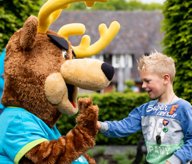 Een lachende jongen geeft een high five aan de grote poot van parkmascotte Spot op vakantiepark Landgoed de Scheleberg.