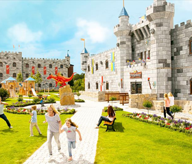 Kinderen spelen in de kasteeltuin van het LEGOLAND hotel, met op de voorgrond een grote rode LEGO draak en de kasteelgebouwen erachter.