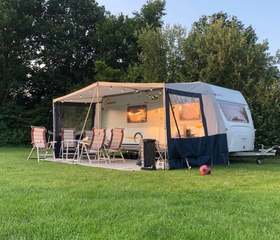 Een caravan met voortent staat op een ruime en groene kampeerplek op de camping van Marveld Recreatie.