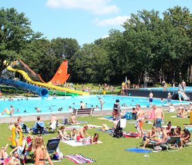 Een grote, zonnige ligweide vol met gezinnen die ontspannen op handdoeken naast de zwembaden van Waterspeelpark Splesj.