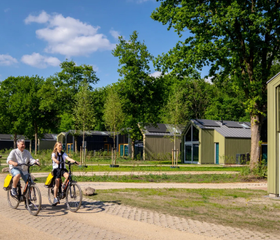 Een gezin fietst vrolijk over een pad op vakantiepark Olde Kottink, langs de moderne vakantielodges.