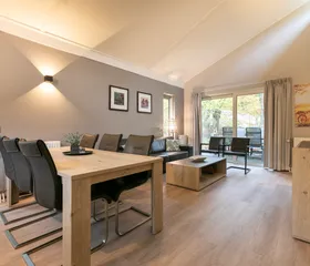 Ruime en lichte woonkamer met een grote eettafel en een comfortabele zithoek in een bungalow op Parc de Berkenhorst.