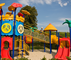 Een groot en kleurrijk speelkasteel met glijbanen, een klimwand en een touwbrug in de zandspeeltuin van Parc de IJsselhoeve.