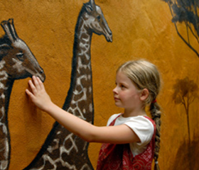 Meisje met vlechten raakt een muurschildering van giraffen aan in het Afrikaans gethematiseerde Hotel Matamba in Phantasialand.