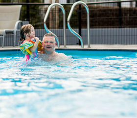 Een gezin met jonge kinderen heeft waterpret in het zwembad van Recreatiepark Beekbergen, omringd door ligstoelen.