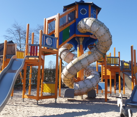 Een groot en kleurrijk houten speeltoestel op Recreatiepark de Boshoek met een hoge uitkijktoren en een lange, kronkelende tunnelglijbaan.