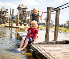 Kinderen spelen op een houten vlot bij het avontuurlijke speeleiland en poedelen met hun voeten in het water van het Esmeer.