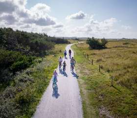 Luchtfoto van een familie die fietst over een fietspad door het uitgestrekte duinlandschap nabij Bergen.
