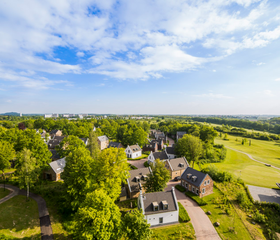 Luchtfoto van de luxe vakantiehuizen van Dormio Resort Maastricht, omgeven door bomen en groene velden.