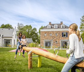Kinderen en een moeder spelen samen op een grote houten wipwap in een van de speeltuinen op Dormio Resort Maastricht.