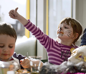 Een vrolijk meisje met haar gezicht geschminkt als een kat doet mee met de kinderanimatie in het Rhön Park Hotel.