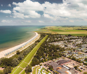 Luchtfoto van het brede zandstrand en de vakantiehuisjes van Roompot Beach Resort aan de Zeeuwse kust.