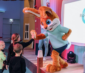 Kinderen geven een high five aan mascotte Koos Konijn die op het podium staat tijdens een show in de Koos Kids Club.