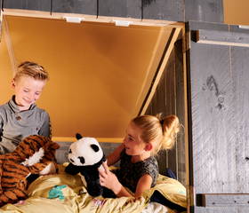 Een broer en zus spelen met hun knuffels in de knusse, houten bedstee van hun safaritent op Vakantiepark Sallandshoeve.