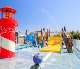 Kinderen spelen in de waterspeeltuin met een grote vuurtoren en glijbaan op Strandpark De Zeeuwse Kust in Zeeland.