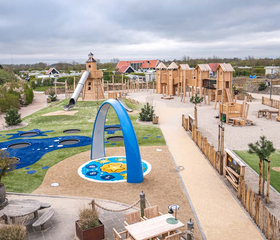 Overzicht van de grote buitenspeeltuin van zand en hout met klimtoestellen en trampolines bij Strandpark De Zeeuwse Kust.