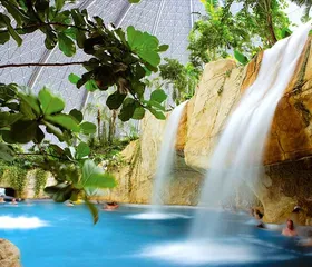 Een grote waterval stort in het helderblauwe water van de Bali Lagune, omringd door rotsen en tropische planten in de koepel van Tropical Islands.