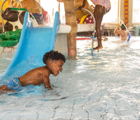 Een klein jongetje heeft waterpret bij de peuterglijbaan in het kinderbad van het overdekte zwembad op Vakantiepark Aquadelta.