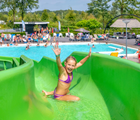 Een meisje glijdt vrolijk van de bochtige groene waterglijbaan in het waterpark