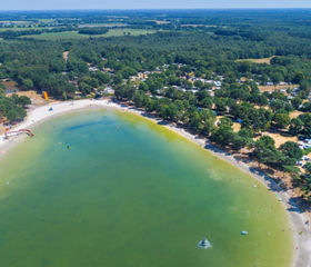 Helderblauw water en een uitgestrekt zandstrand bij de recreatieplas van Vakantiepark De Bergen, gezien vanuit de lucht.