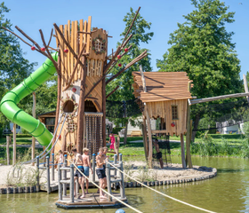 Een hoge houten klimtoren met een groene glijbaan in de buitenspeeltuin