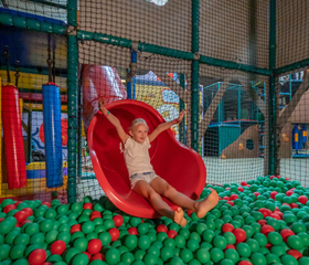 Een kind glijdt in de grote ballenbak vol gekleurde ballen