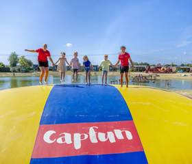 Kinderen springen op de grote gele airtrampoline bij de zwemvijver