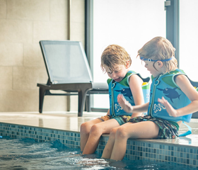 Twee jongens met zwemvestjes en duikbrillen zitten met hun voeten in het water aan de rand van het binnenzwembad van Vakantiepark De Krim.