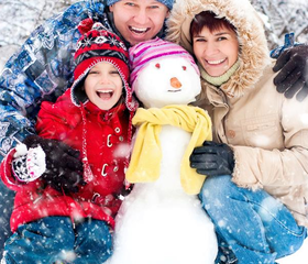 Een lachende familie met kinderen die in de winter een vrolijke sneeuwpop met een gele sjaal knuffelen op Vakantiepark Hasseröder.