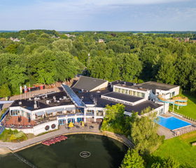 Luchtfoto van Vakantiepark Hunzedal, waarop de centrale gebouwen, de recreatieplas, het zwembad en de groene, bosrijke omgeving in Drenthe te zien zijn.
