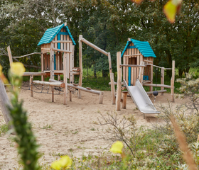 Een avontuurlijke houten speeltuin met een glijbaan en klimtoestellen, gelegen in het zand op Vakantiepark Kijkduin.
