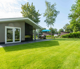 Een modern chalet met een groot, zonnig grasveld ervoor, waar kinderen alle ruimte hebben om te spelen op Vakantiepark Leuvert.