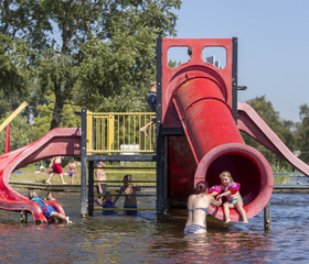 Kinderen glijden van een grote rode waterglijbaan die uitkomt in de recreatieplas bij Vakantiepark Marina Beach.