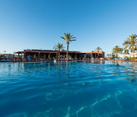 Het grote, helderblauwe zwembad van vakantiepark Parque Cristobal, omringd door palmbomen onder een strakblauwe hemel.